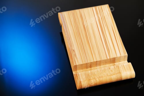 Preview: Wooden desktop mobile phone holder with hand-held phone isolated on blue black background.