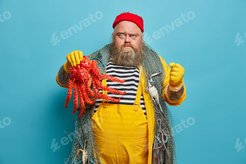 Preview: Photo of irritated fisherman holds octopus, clenches fist angrily, being angry with someone, wears r