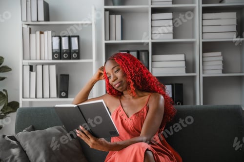 Preview: Young woman reading a book sitting on a sofa in the living room
