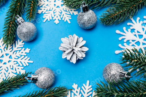 Preview: top view of snowflakes, silver baubles and spruce with cone on blue background