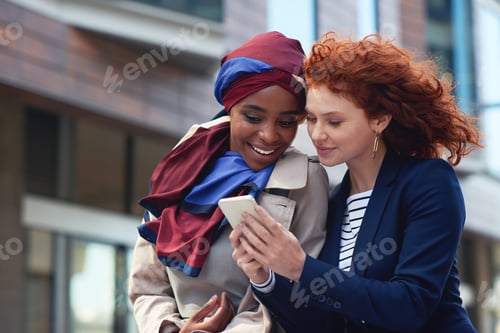 Preview: Two business women friends using smartphone looking at mobile phone in city