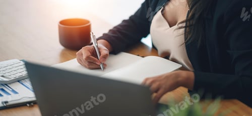 Preview: Closeup image of businesswoman hand writing note and working on laptop computer at office.