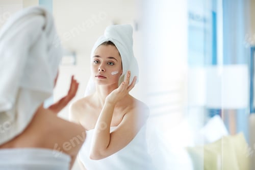 Woman Applying Moisturizer to Face in Mirror