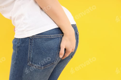 Preview: Woman holds her ass on yellow background. Hemorrhoids concept