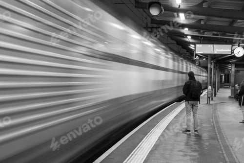 Preview: Greyscale shot of a man waiting for a train in the station and a blurred train in the motion