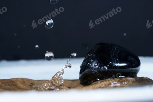 Preview: Closeup shot of shiny obsidian rock in water with droplets of water