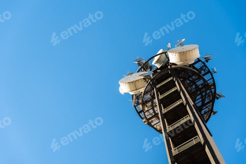 Preview: Telecommunications tower isolated on blue sky background, with dozens of antennas.