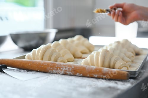 Preview: Pastry chef smearing egg yolk on raw bun with silicone brush closeup