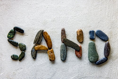 Preview: Word SAND is written using colored stones on a white sandy surface