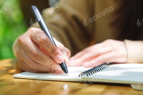 Preview: Closeup image of a woman writing on a notebook in the outdoors
