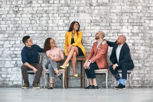 Preview: Beautiful cheerful professional woman wearing eyeglasses seated with male co-workers and team leader