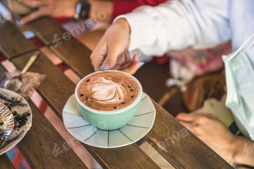 Preview: Woman hand holding a cup of hot chocolate with pattern from fresh milk