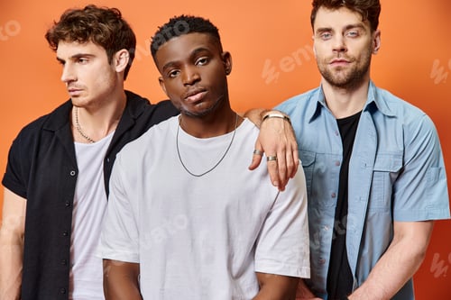Preview: good looking multiracial male models in street attires looking at camera on orange backdrop, fashion