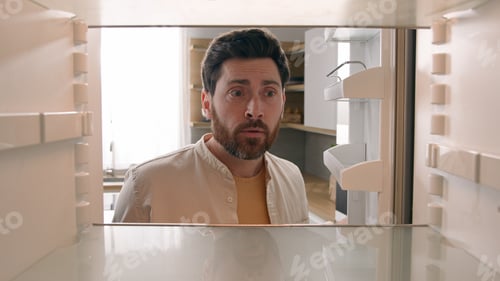 Preview: Hungry Caucasian bachelor man looking for food in empty fridge finding no meal products feeling sad