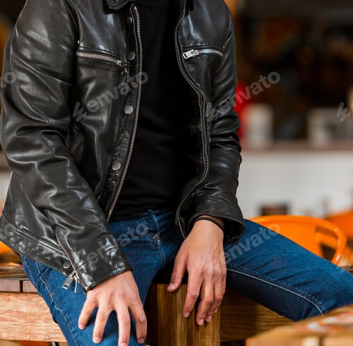 Preview: Shallow focus of an adult male wearing jeans with a leather jacket and sitting on the table
