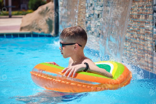 Preview: Happy child boy swimming on inflatable circle in swimming pool on sunny summer day during tropical