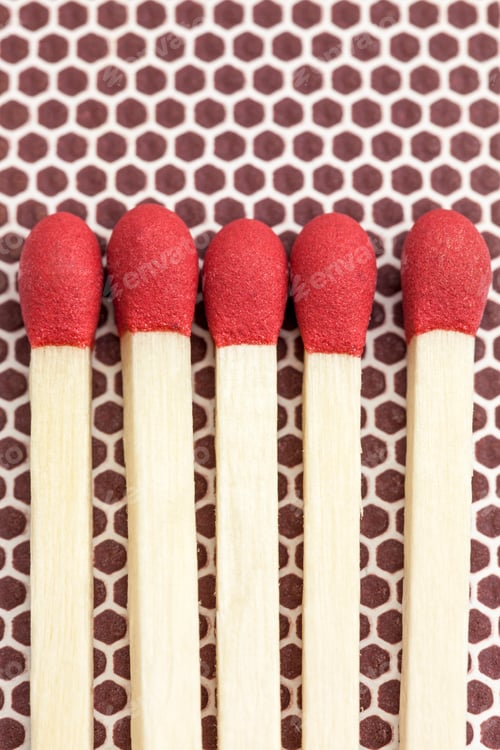 Preview: Five unlit wooden matchsticks with red heads arranged side by side on a brown matchbox surface