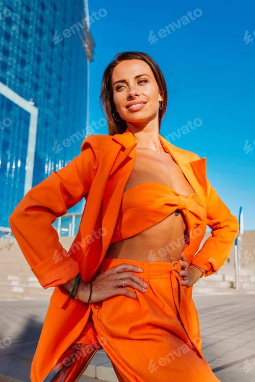 Preview: Beautiful woman in an orange suit posing with hands on waist