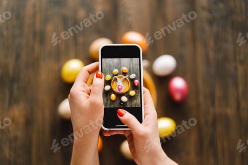 Preview: Woman holding mobile phone and making photo of eggs painted for Easter isolated on wooden background