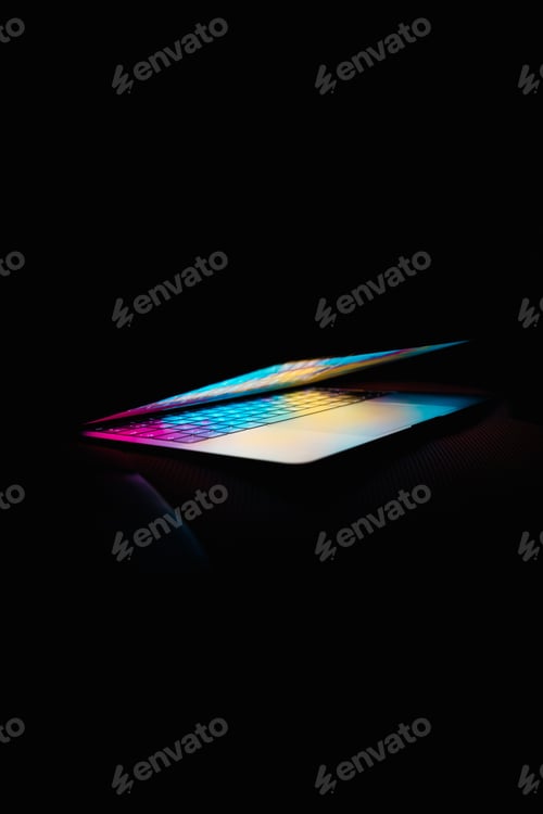 Preview: Vertical shot of a half-opened laptop with colorful lights in a dark setting