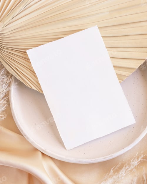 Preview: Blank card on plate on dried palm leaf and beige silky fabric close up, greeting or wedding mockup