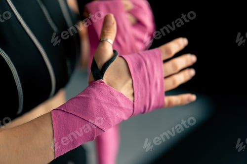 Preview: close up at a boxing fight club young girl in a black sweatshirt wraps pink elastic bandages for