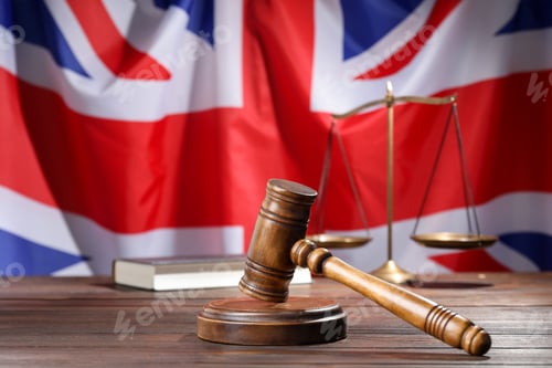Preview: Judge's gavel, book and scales on wooden table against flag of United Kingdom, closeup