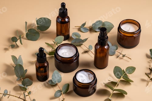 Preview: Set of beauty products in amber glass bottles and jars on beige background with eucalyptus leaves.