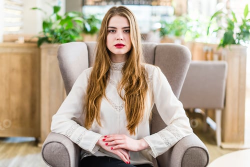Preview: Beautiful young girl with professional makeup and hairstyle sitting in restaurant.