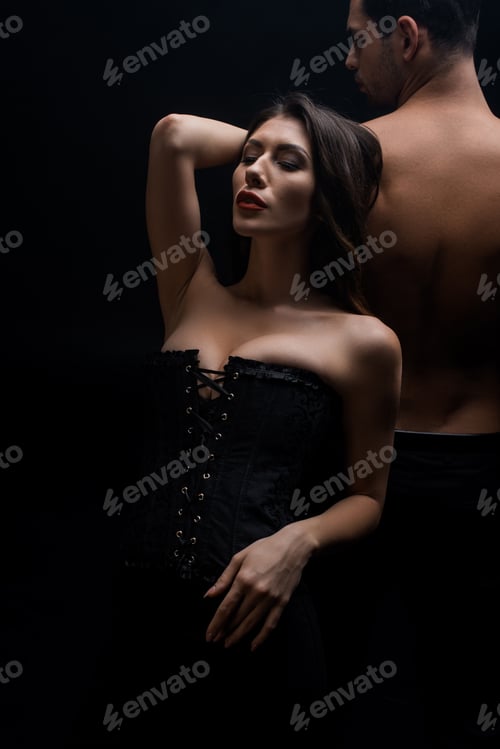 Preview: Sexy woman in corset standing by shirtless man isolated on black