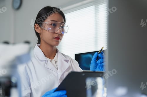 Preview: Scientist analyzing data on computer in modern laboratory wearing lab coat and safety glasses