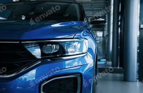 Preview: Front part of brand new modern blue car. Parked at showroom. Reflection in the headlights