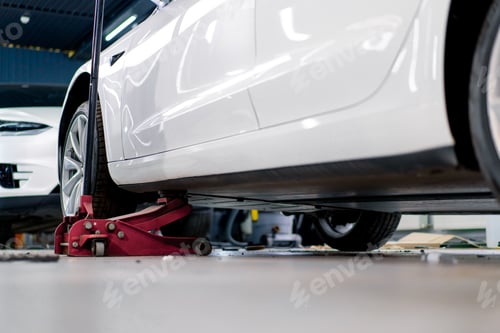 Preview: White luxury car being lifted with a red wheel change jack at a car service during detailing