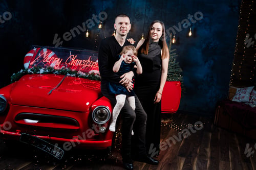 Preview: mom, dad and little daughter in love in Christmas are hugging near a red retro car with New Year's g