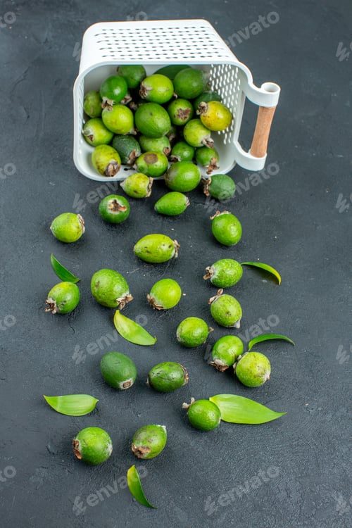 Preview: bottom view fresh feijoas scattered from plastic basket on dark background
