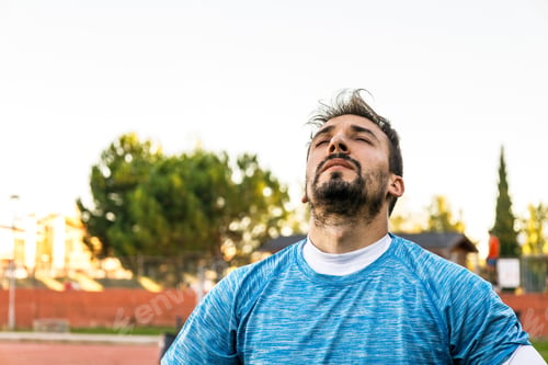 Preview: man catching air and breathing deeply after doing his workout outdoors, closeup view