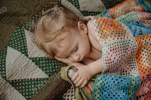 Preview: Cute baby sleeps peacefully in crib with handle under his cheek