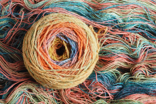 Preview: Ball of yarn from pure organic sheep's wool on an unwound skein of woolen threads. Rainbow color.