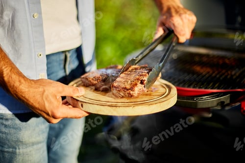 Preview: Man put down meat on a wooden board ready to eat grilled steak meat,