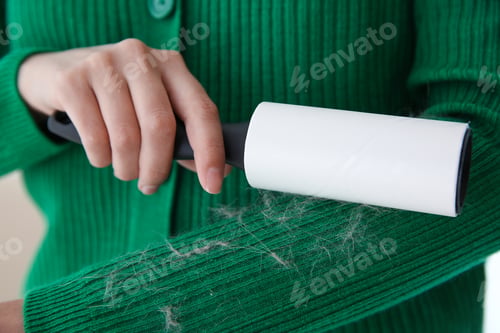 Preview: Woman removing hair from green knitted jacket with lint roller on light background, closeup