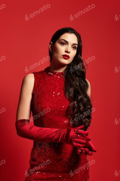 Preview: Captivating young woman in striking red attire with elegant makeup in studio setting