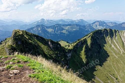 Vorschau: Panoramablick auf üppig grüne Berge unter teilweise bewölktem Himmel.