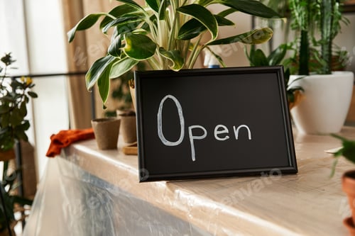 Preview: Sign with word Open among lush greenery in studio.