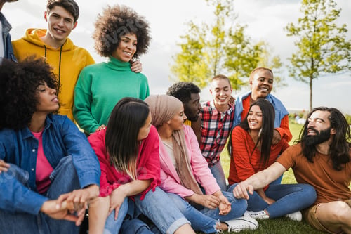 Preview: Happy diverse people having fun outdoor sitting on grass at city park - Focus on arabian girl face