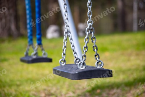 Preview: Soft focus of an empty swing set at a park against a blurry greenery