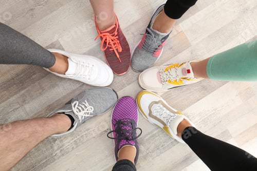 Preview: Closeup of athletes wearing sports shoes and standing in circle on wooden floor, top view