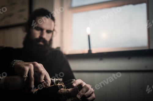 Preview: A man sitting alone in a room pouring himself a glass of whisky. A lit candle.