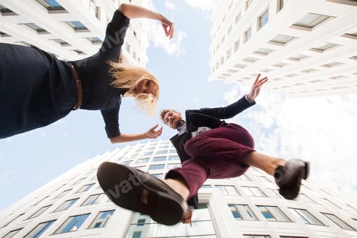 Preview: Cheerful young couple fooling around, jumping on the background of the building. Bottom view