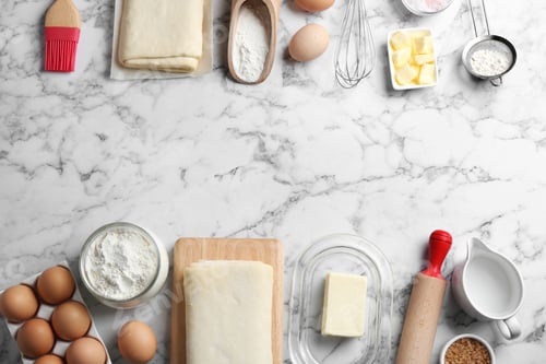 Preview: Frame made with puff pastry dough and ingredients on white marble table, flat lay. Space for text