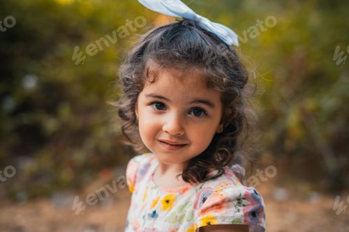 Preview: Young girl in a floral outfit with a bow in her hair, looking at the camera and smiling slightly
